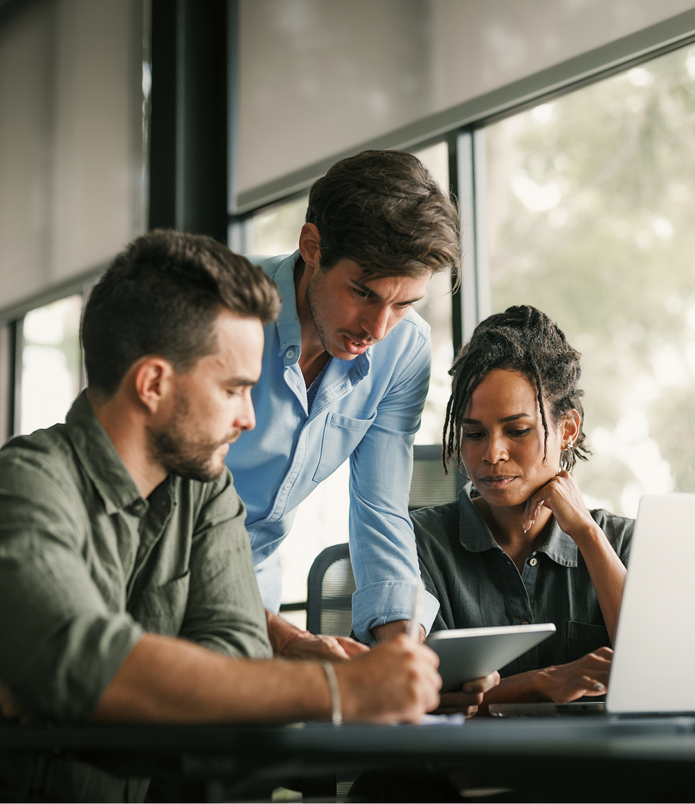 Three professionals collaborating at a desk with laptop and tablet